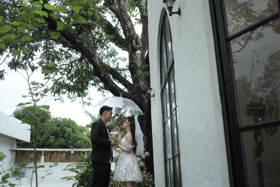 John and Alyssa close under an umbrella by the arched window